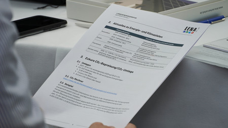 Eine Person hält ein Blatt Papier mit den Themen Klimaschutz und CO2-Bepreisung, rechts oben das Logo der Landesenergieagentur Sachsen-Anhalt GmbH (LENA)