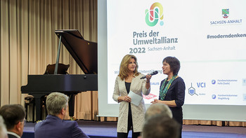 Moderatorin und Juryvorsitzende, im Hintergrund Logo der Umweltallianz und Schriftzug Preis der Umweltallianz Sachsen-Anhalt 2022 