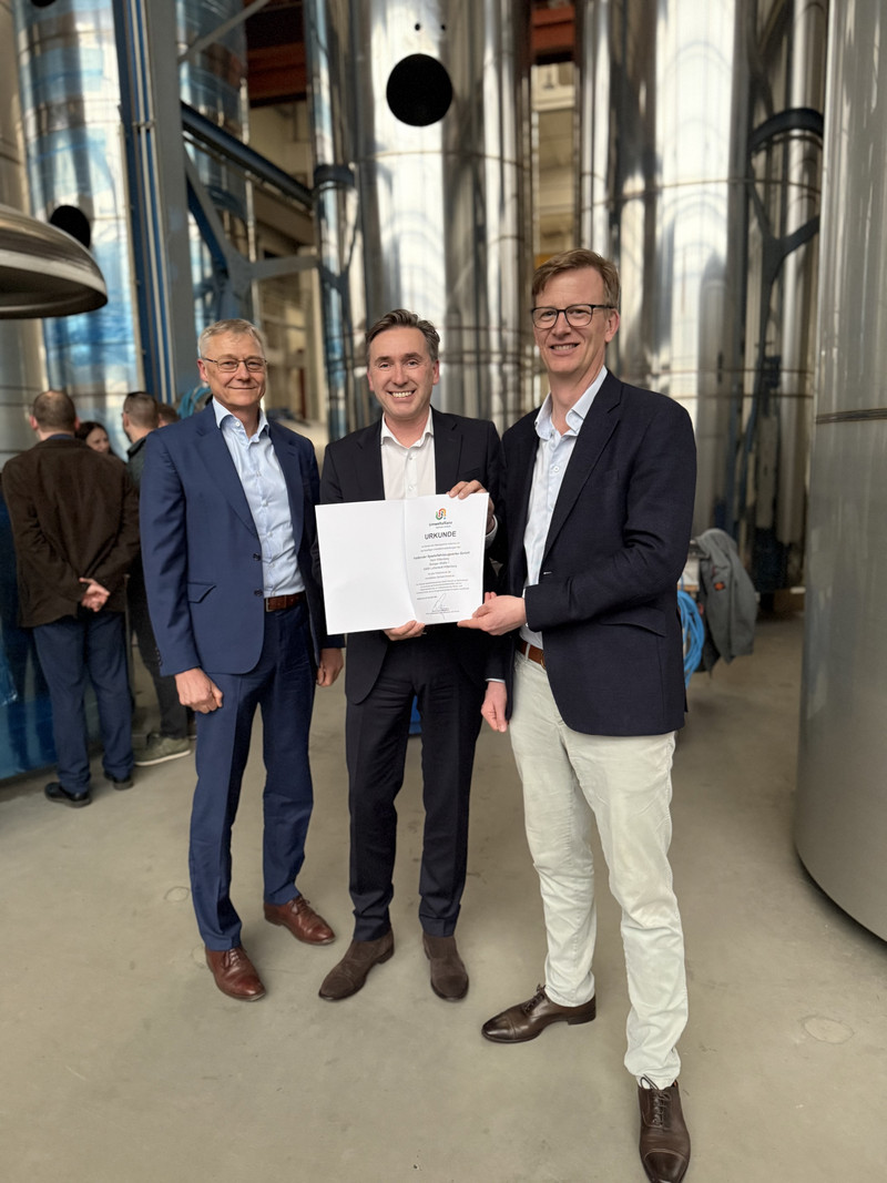 Staatssekretär Wünsch übergibt die Urkunde über die neue Mitgliedschaft in der Umweltallianz Sachsen-Anhalt in einer Werkshalle.